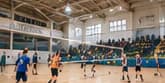 Bagian dalam gedung olahraga yang telah direnovasi, memperlihatkan para siswa bermain bola voli di lapangan dengan tribun di latar belakang