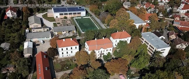 Napsütötte román kori kőárkád, mögötte a Balaton, a túlparti hegyek és a lemenő nap; jobbra kőpillér vésett latin felirattal