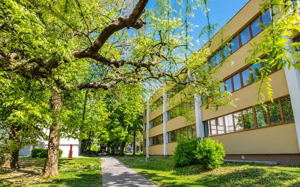 Krémszínű, erkélyes kollégiumi épület fák között