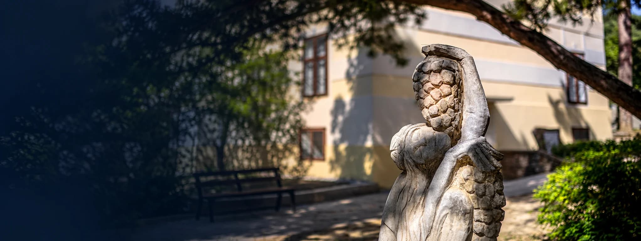 Balatoni panoráma a magasból: előtérben lombok és erdő, piros tetős házak, kéttornyú templom, vitorlások a tavon, a túlparton párás dombok és egy tóparti település.